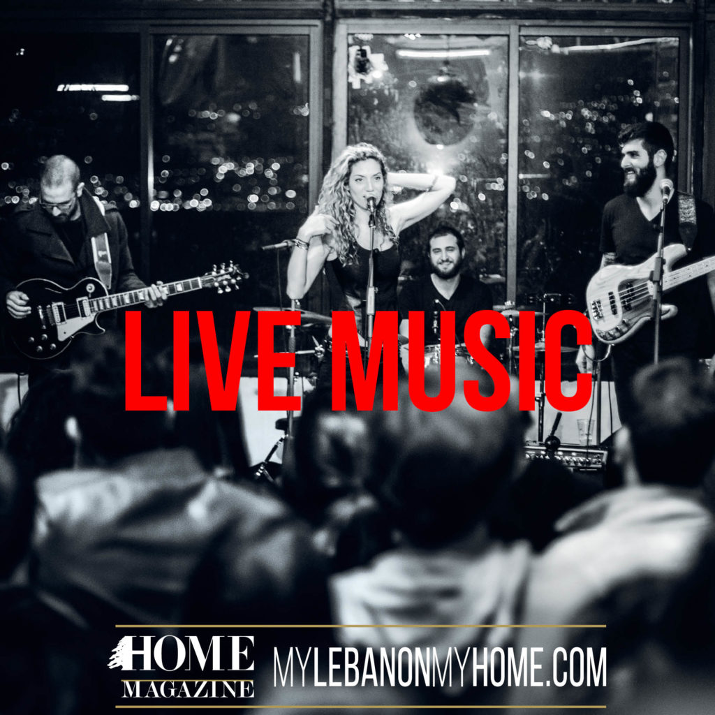 a band with 3 guys holding their guitars and a girl in the middle standing behind a microphone with her hand over her curly hair and the head of people looking at them